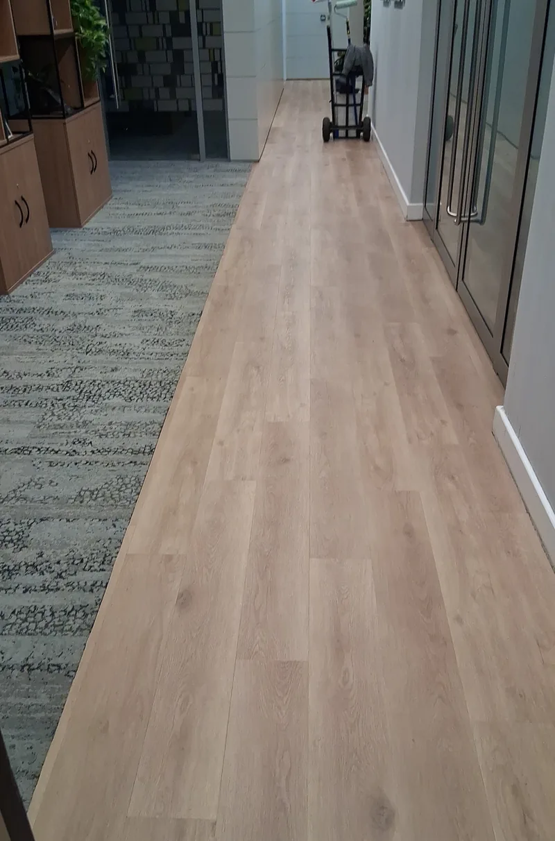 Plank-effect flooring meeting carpet tile in a commercial corridor